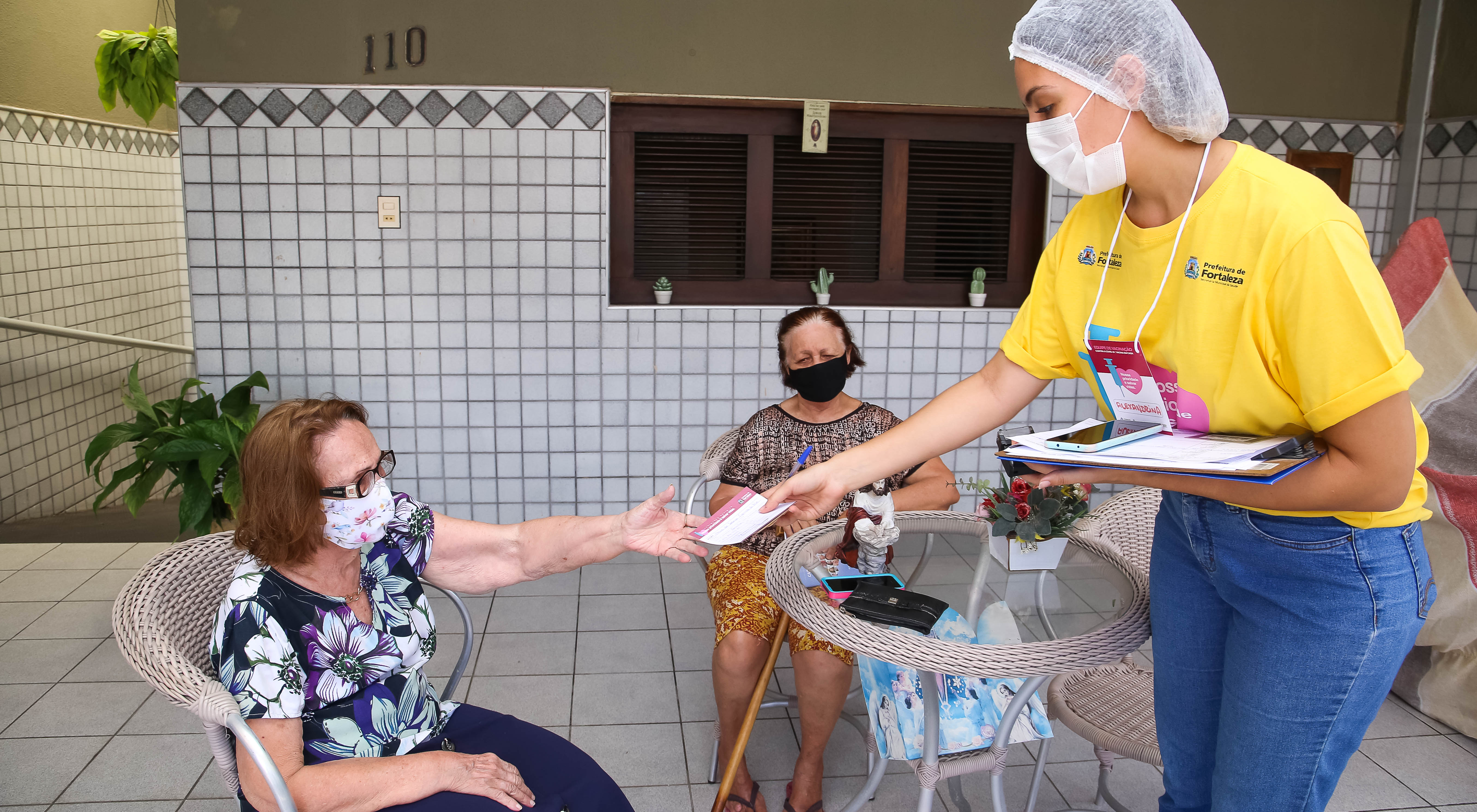 Maria do Socorro Figueiredo recebe o cartão de vacina de uma enfermeira